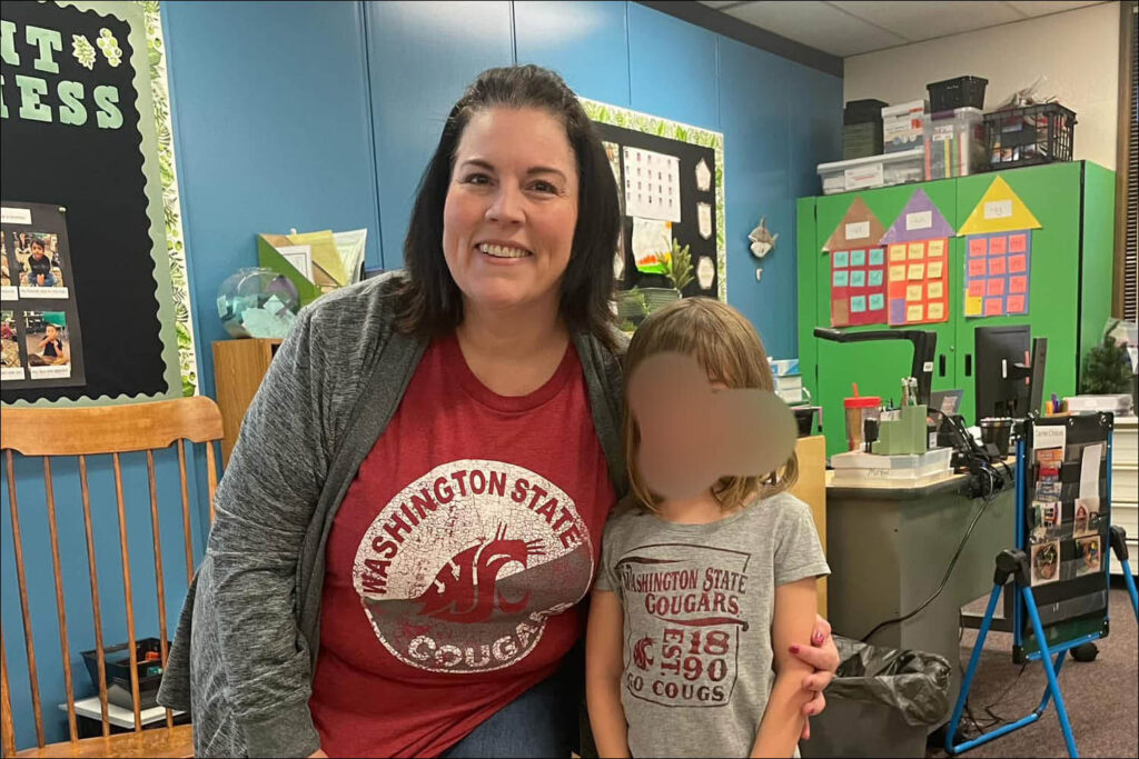 A woman smiling while holding a toddler in a brightly decorated classroom