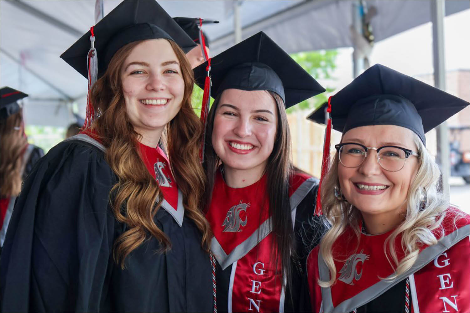 Three graduates in black gowns and caps smiling at a graduation ceremony