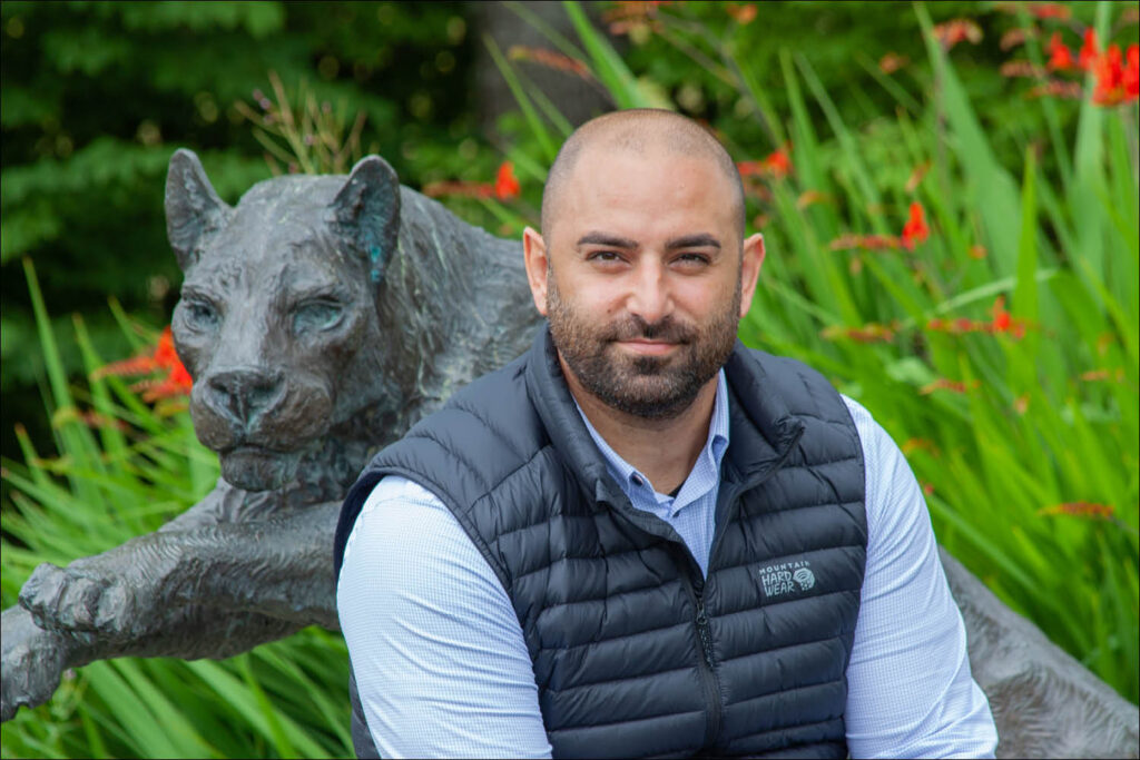 A stone cougar statue surrounded by green foliage on campus