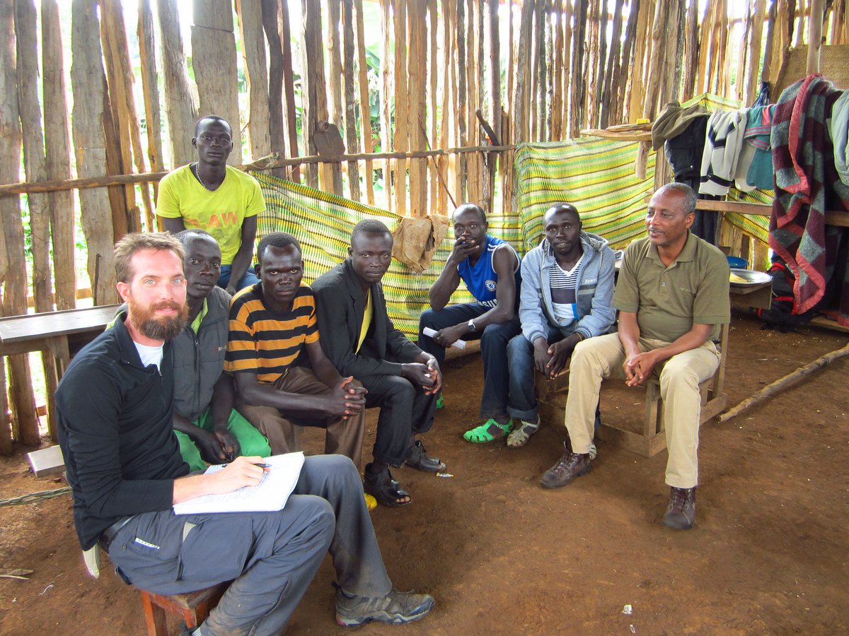 A group sitting together outdoors in a wooded campus area listening to a WSU Vancouver instructor