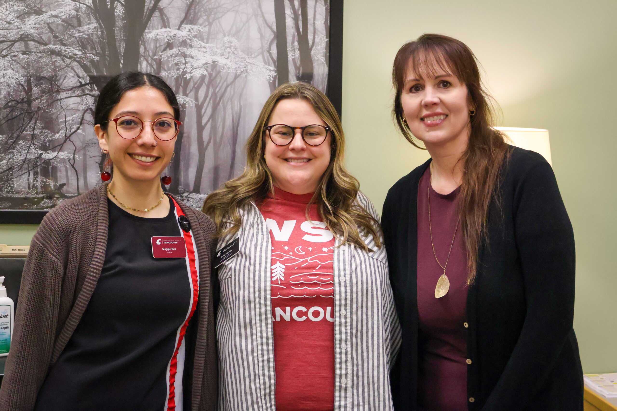 Three women posing for a group photo indoors in front of a banner