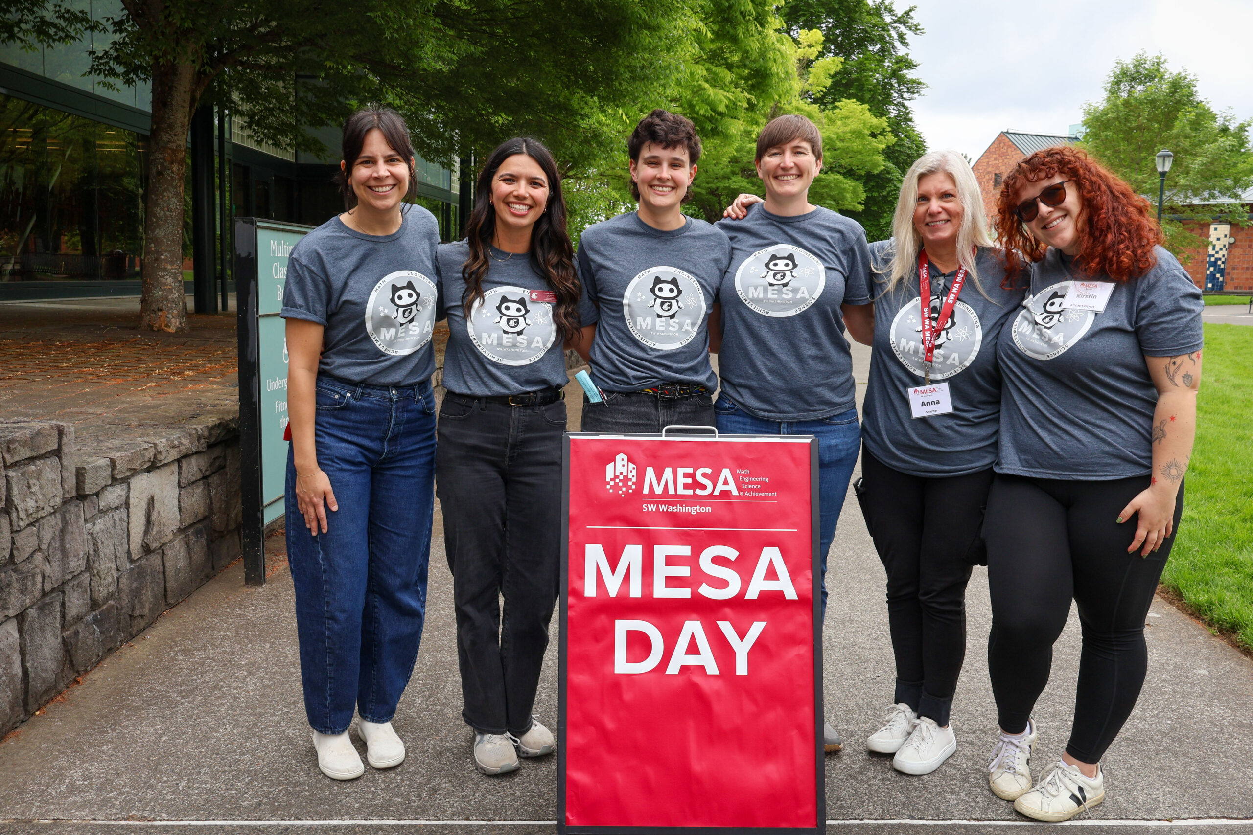 Six students standing outdoors next to a red sign for WSU Vancouver MESA Day