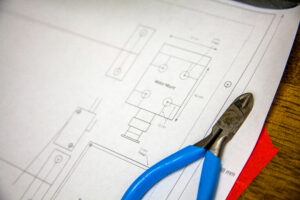 A blueprint or floor plan schematic layout shown next to pliers