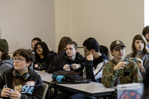 A group of students sitting at desks in a classroom setting listening to a lecture