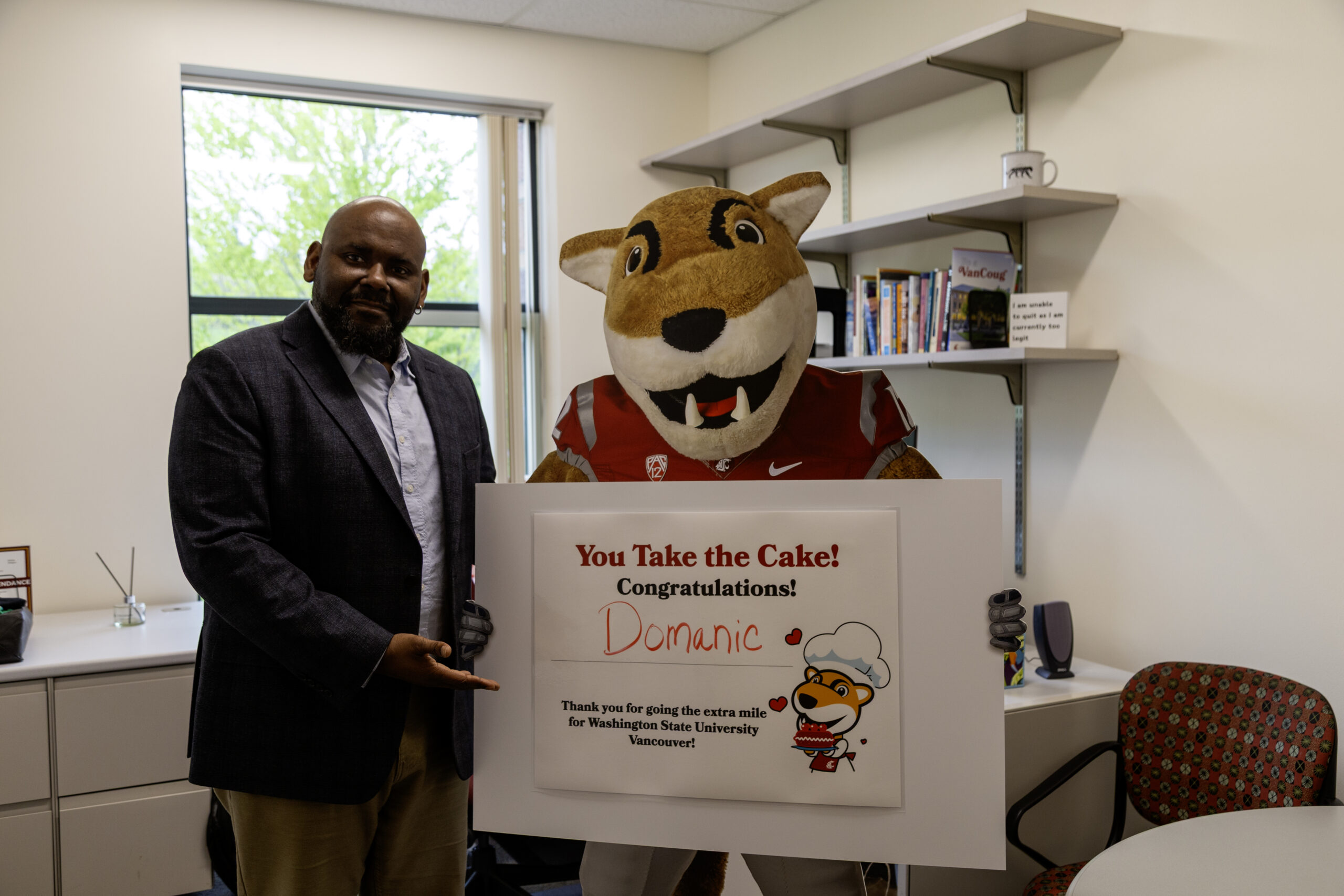 A staff member standing proudly alongside Butch, the WSU mascot, holding a sign outdoors
