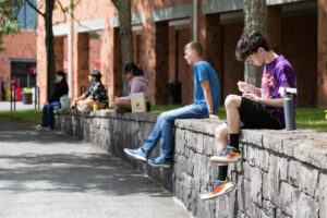Students sitting along a stone ledge outside a brick building on campus