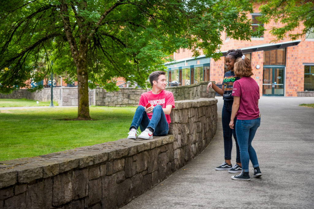 WSU Vancouver students sitting on a stone wall on campus chatting