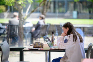 A student working on a laptop at a table outdoors on a sunny day