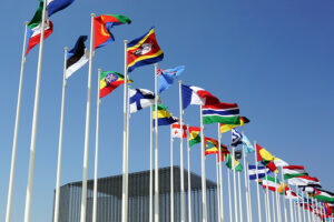 A row of international flags flying on flagpoles against a clear blue sky