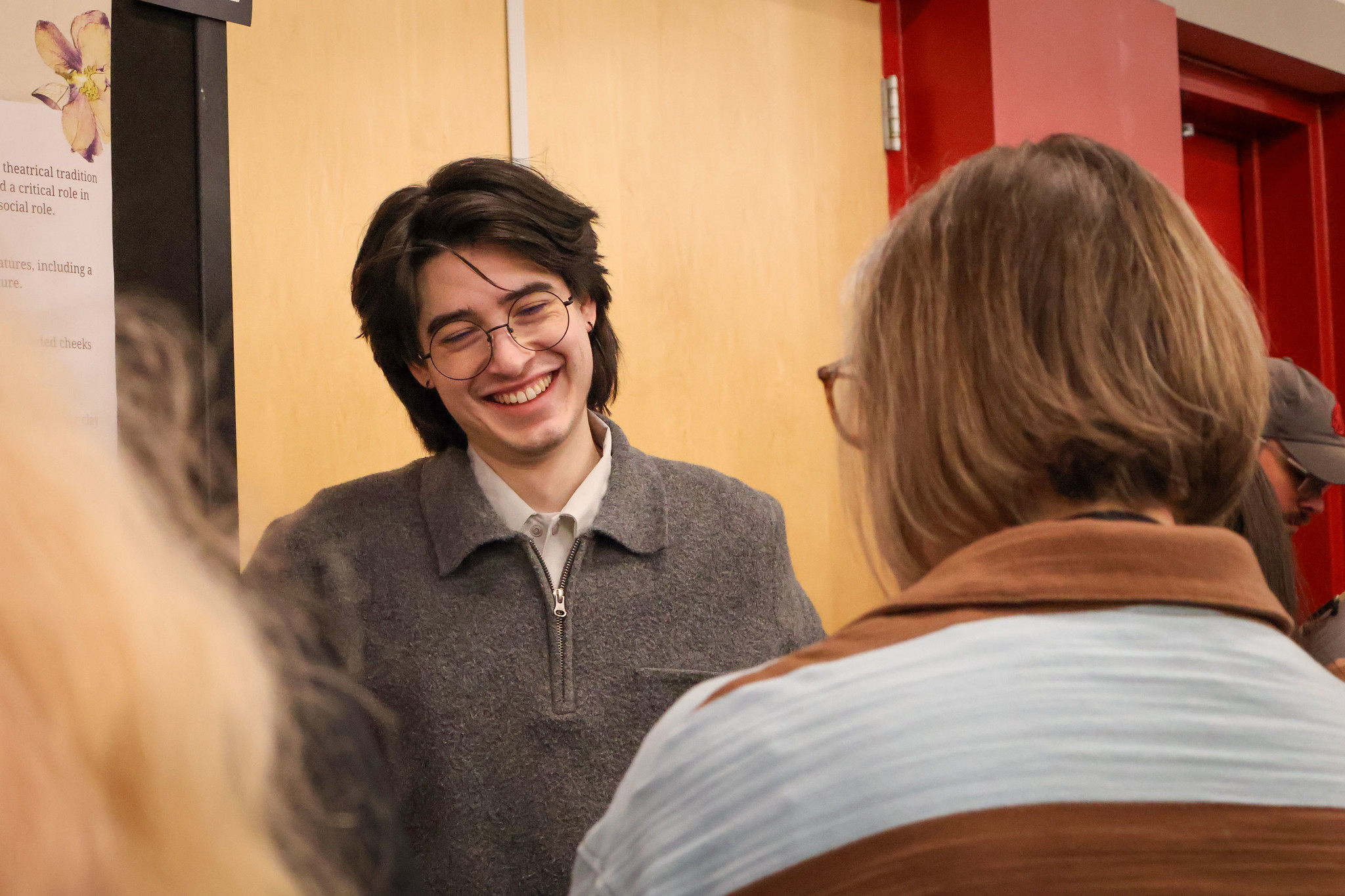 A young man smiling while talking to someone off-camera indoors