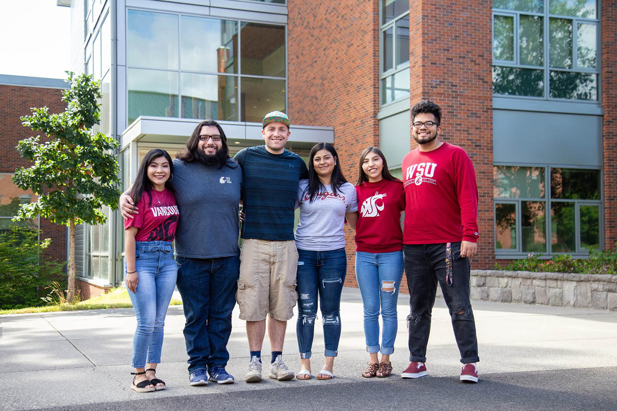 A group of four students posing together outside a university building
