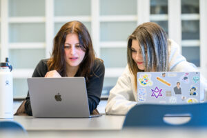 Two female students collaborating on a MacBook laptop in a modern study lounge