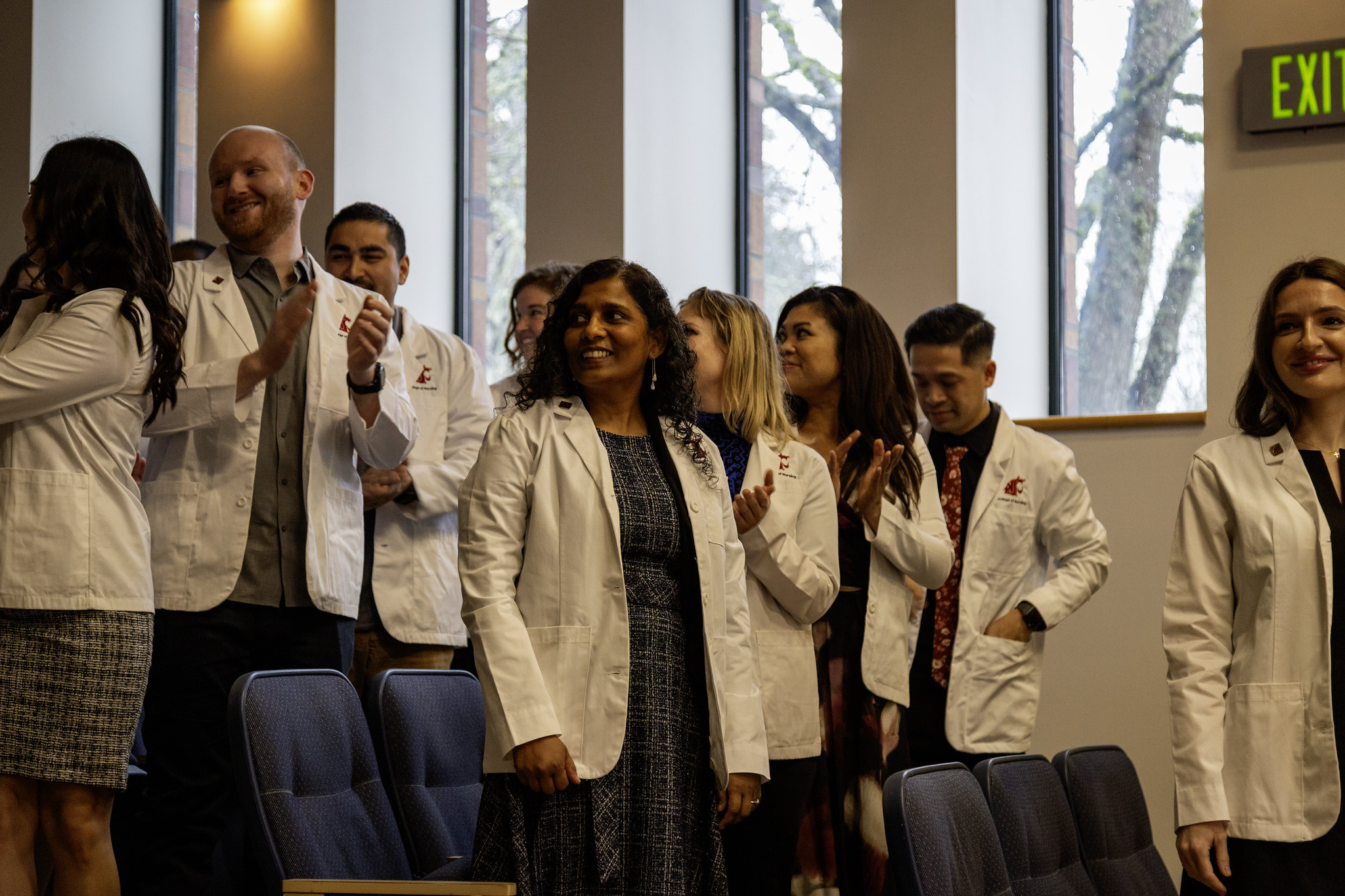 A group of nursing students wearing white medical coats posing together on campus stairs