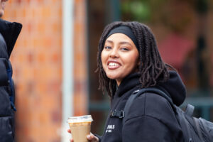A young woman smiling while holding a coffee cup outdoors