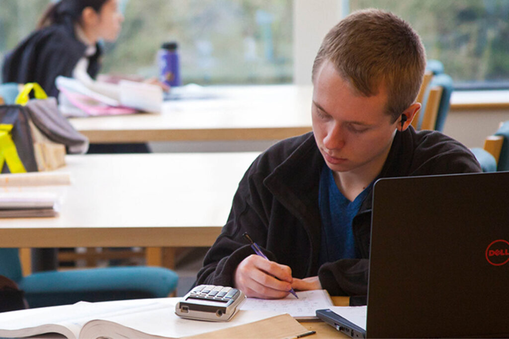 A student focusing and working on a laptop in a library or study space