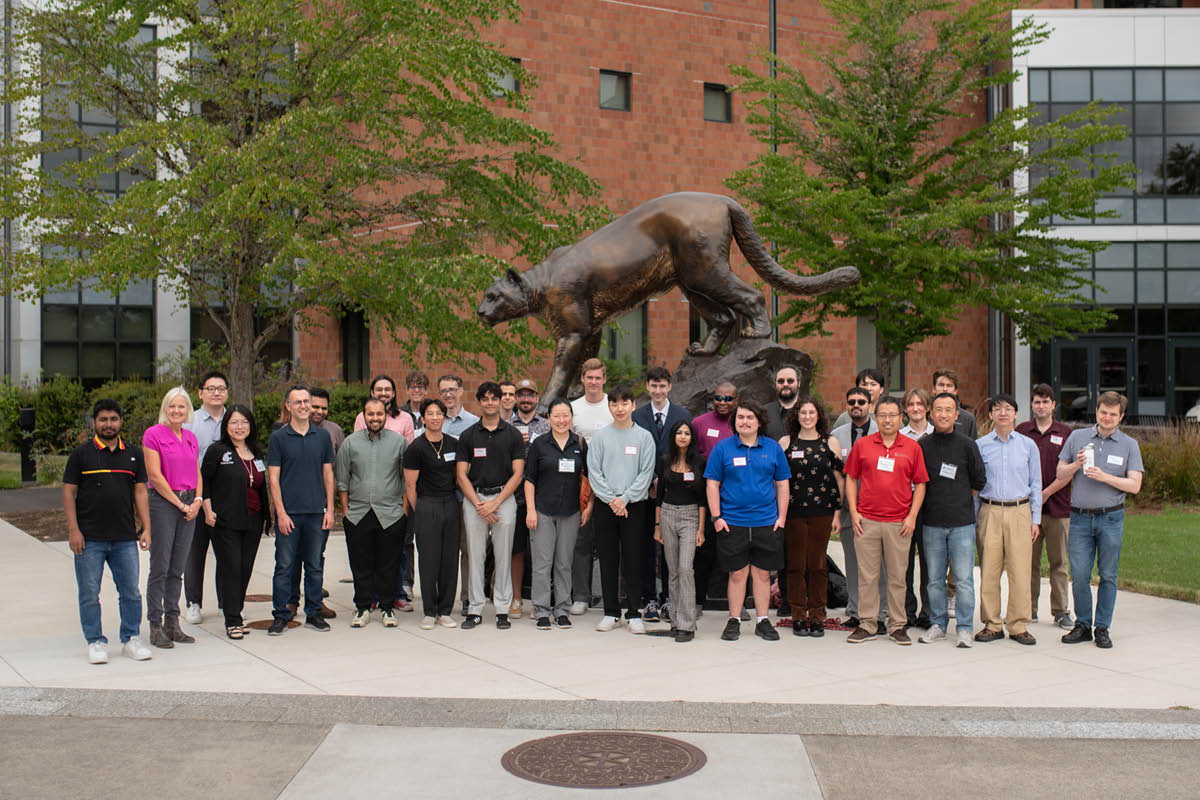 A large group of students posing together outside a brick campus building