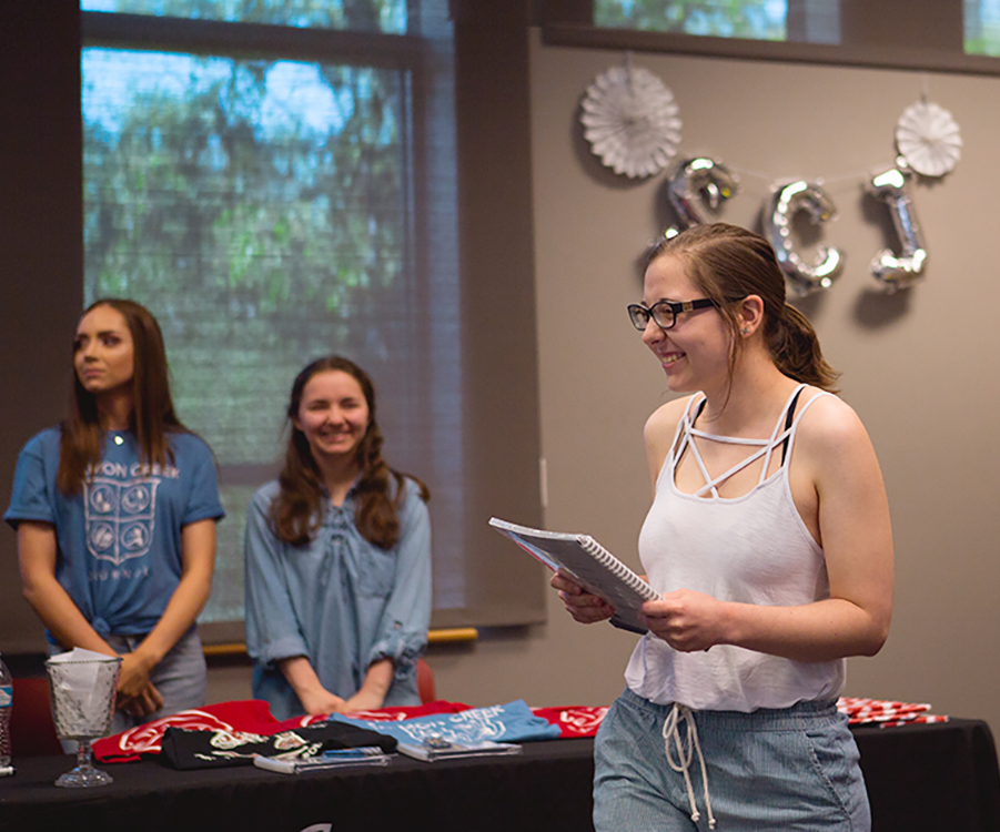 Student presents their work during the Salmon Creek Journal publishing celebration, with student staff members and journal materials visible in the background.