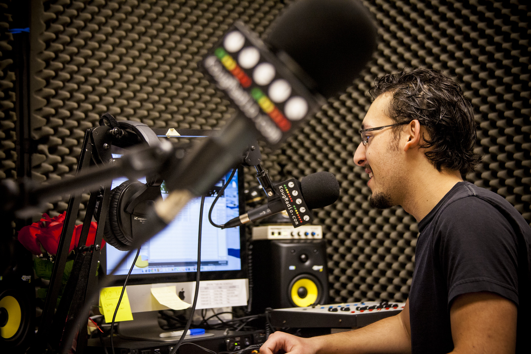 Student operates audio equipment in the KOUG Radio booth, working at a computer with a microphone in front of him.