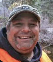 photo of Cager in a baseball cap, black hoody with a big smile on his face.
