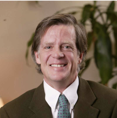 Robert Colllin smiling in a black suit, white shirt and blue necktie.