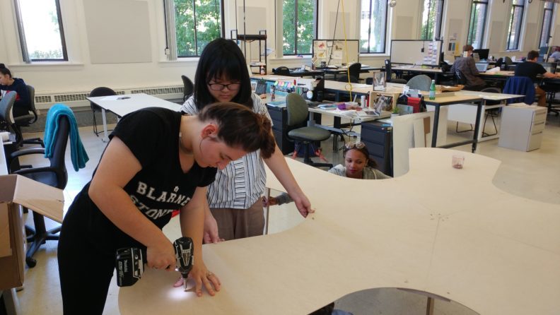 Student in creative studio with a drill working on a project.