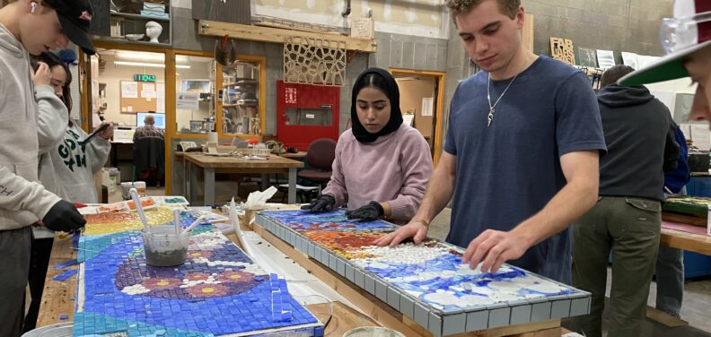 Students assemble mosaics on bench tops they designed for the WSU Kelly Ward Memorial.