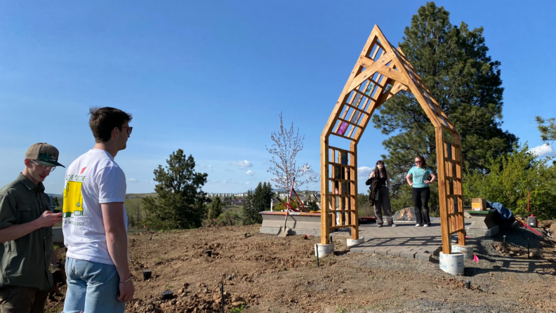 Students standing in a lot with a wooden structure in the center of the photo.