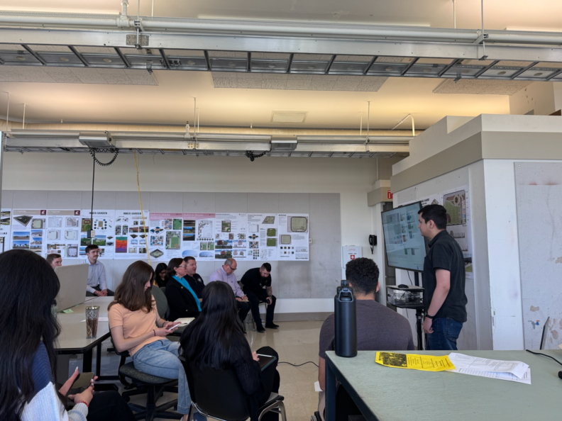 Students seated in a large room watching a presentation on a TV.
