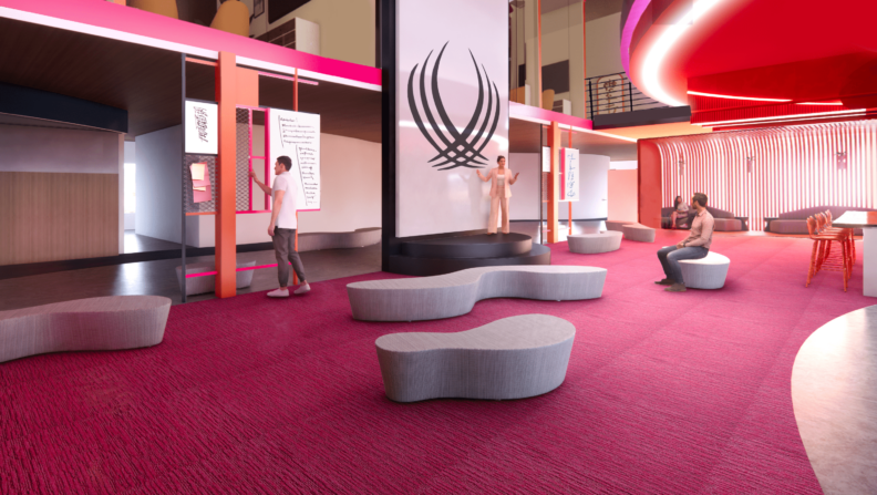 Stage with a large seating area in front. White boards are arranged on both sides of the stage and a person is working in front of the white board on the left side of the stage. A woman is on stage presenting to someone in the seating area.