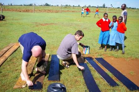 Two men painting boards.