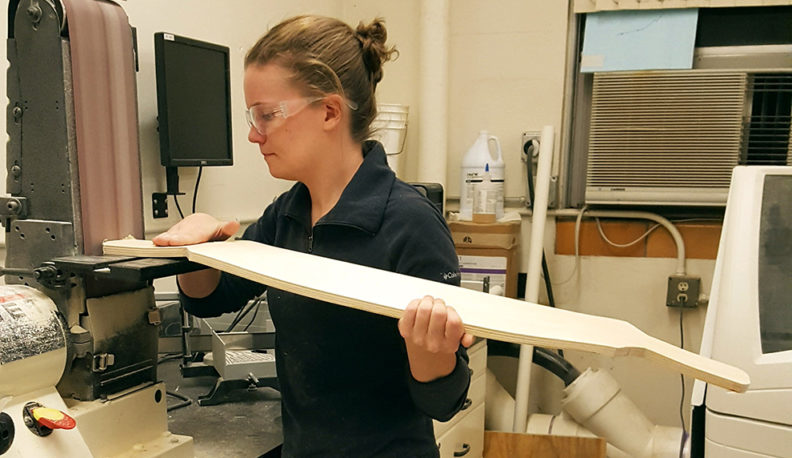 Micah Peyron wearing safety glasses and using a belt sander.