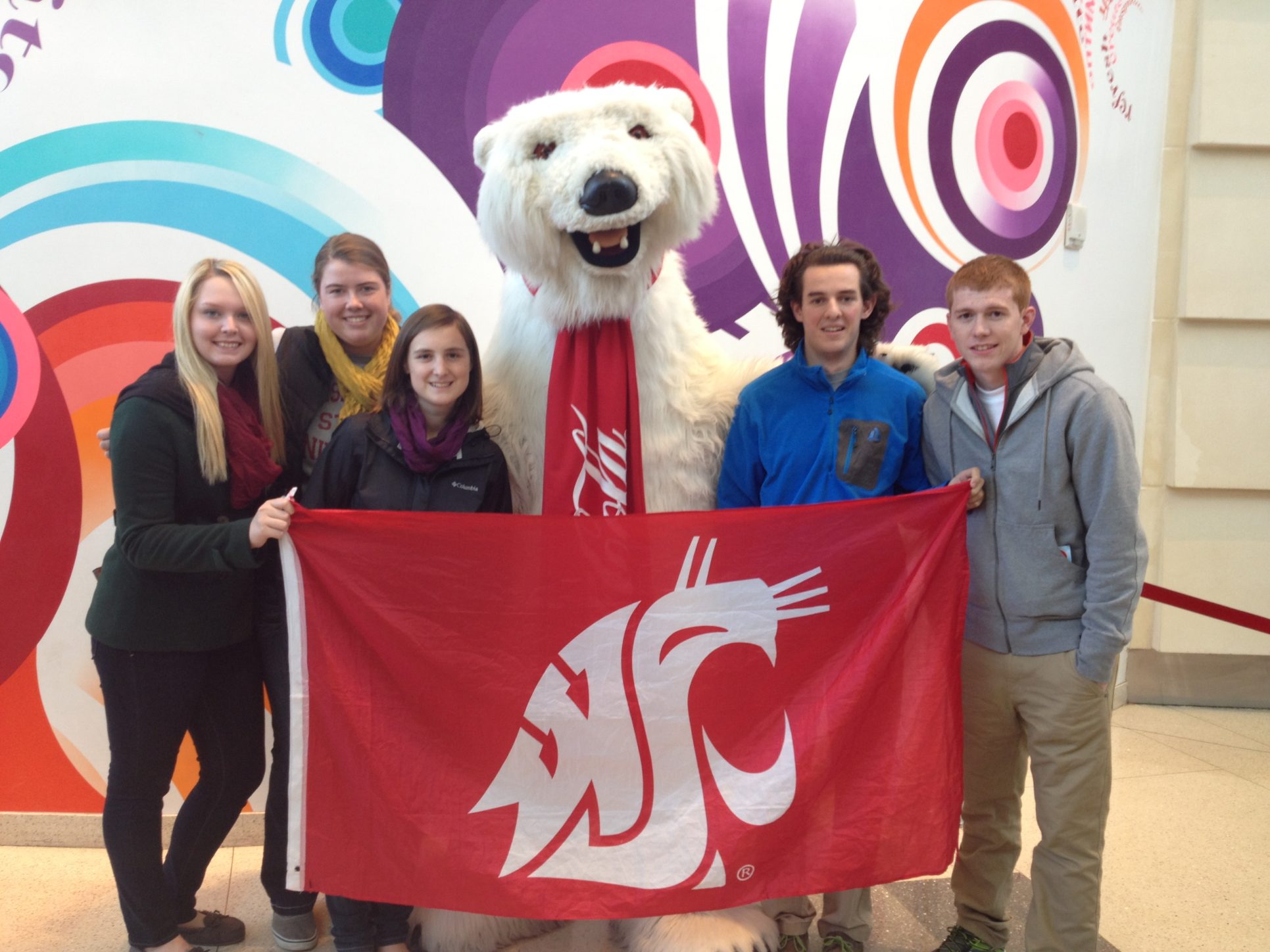 Five students and the Coca-Cola bear mascot pose holding a WSU Cougar flag.