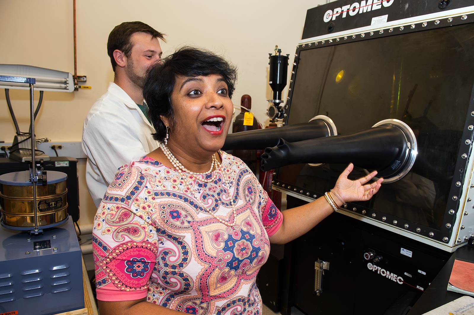 Susmita Bose gestures at a machine while talking excitedly.