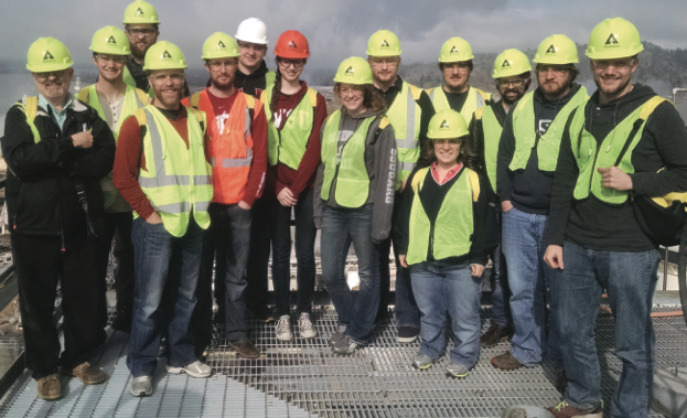 A group of students wearing neon-green safety vests and hard hats, posing for the camera.