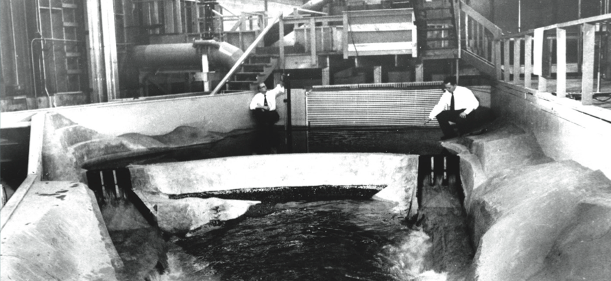 Historical photo of two people by a model of a dam.