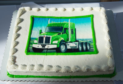 White sheet cake with a photo of a green Kenworth truck on it.