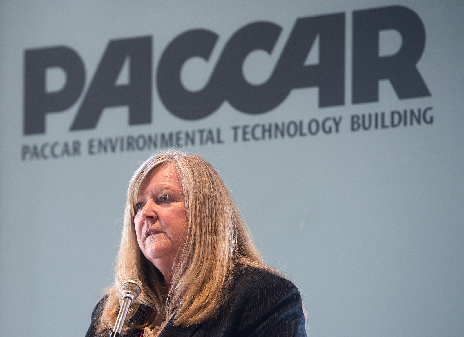 Dean Claiborn in front of a microphone with a wall displaying "PACCAR Environmental Technology Building" behind her.