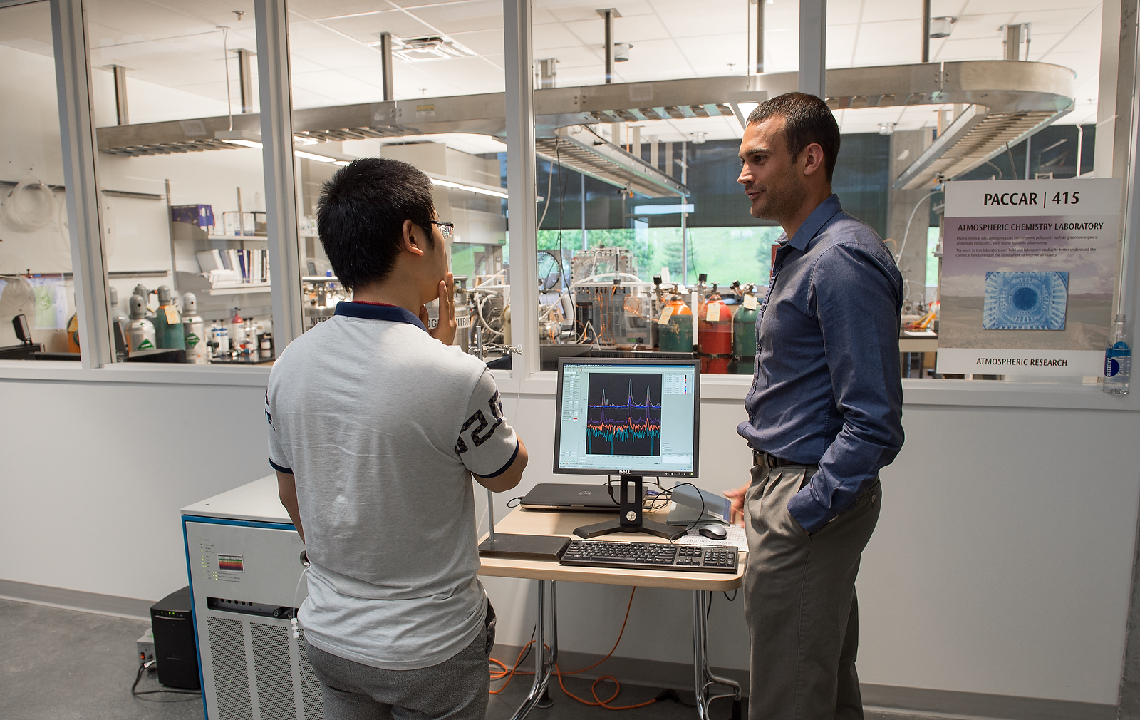 Two men discuss talking by a computer displaying charts.