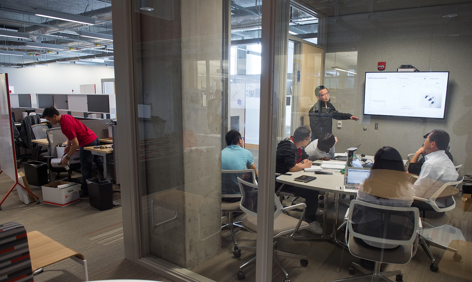 People sitting around a table during a presentation and watching a TV screen.