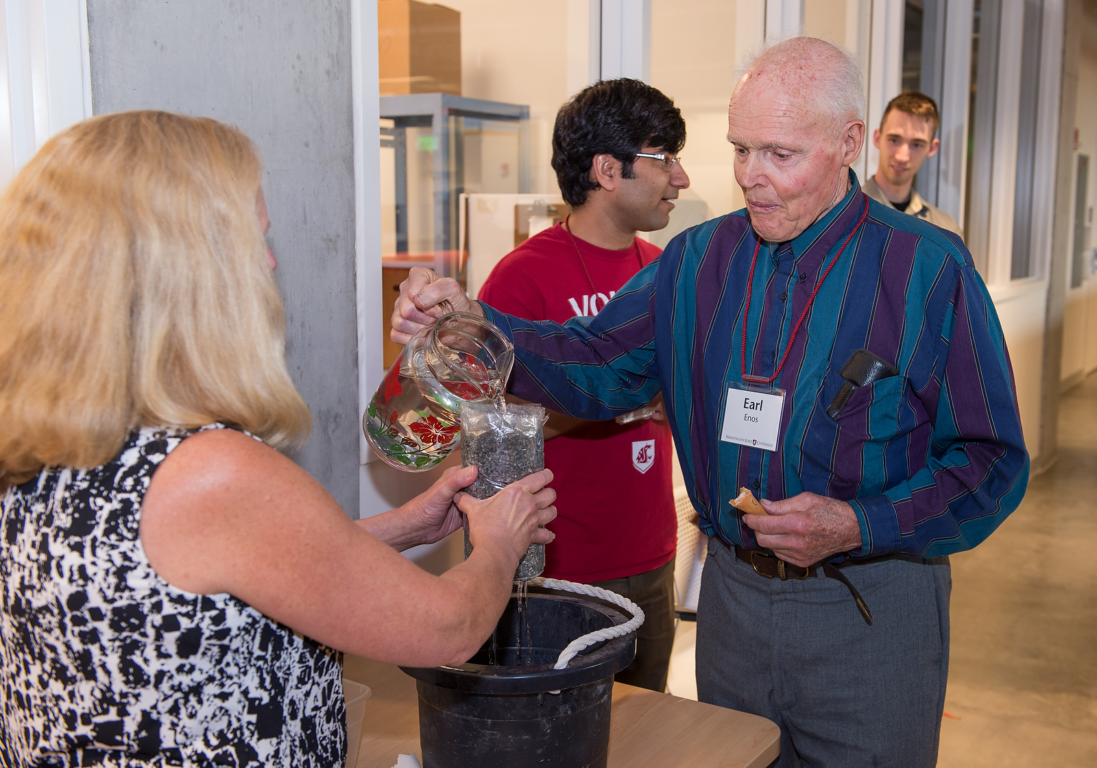 A dedication attendee pours a pitcher of water onto a permeable pavement sample.