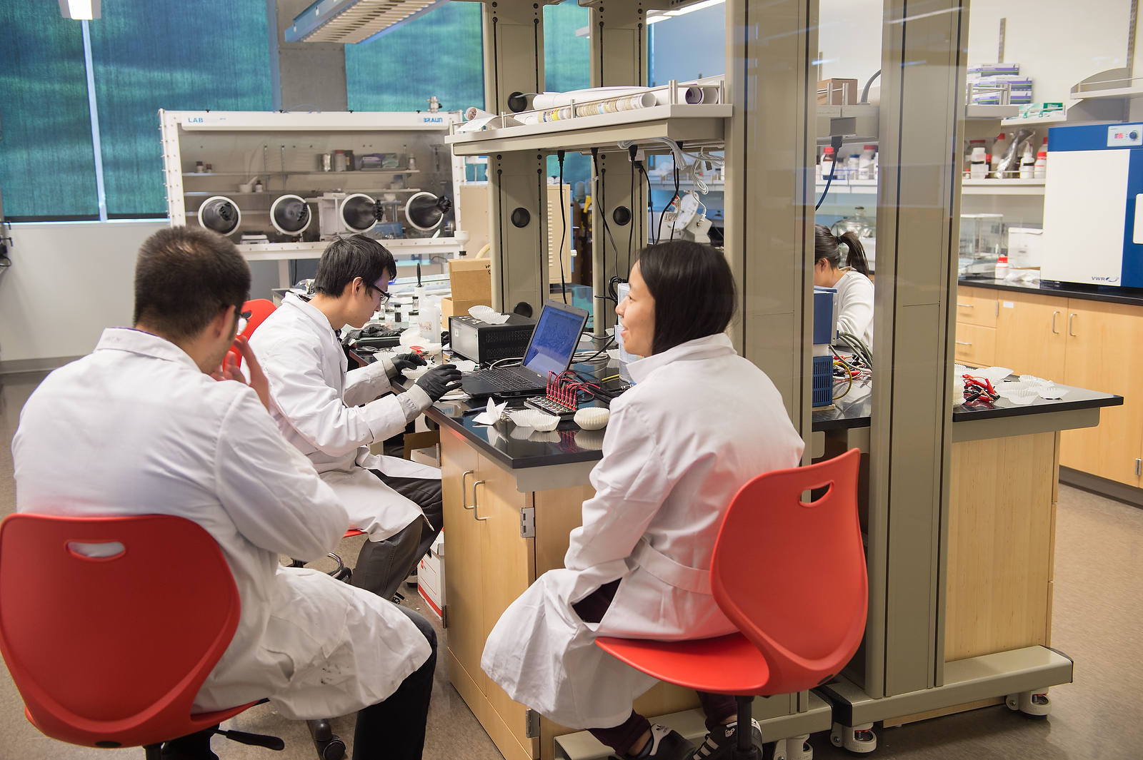 Three researchers wearing white lab coats seated around a workstation with a computer.