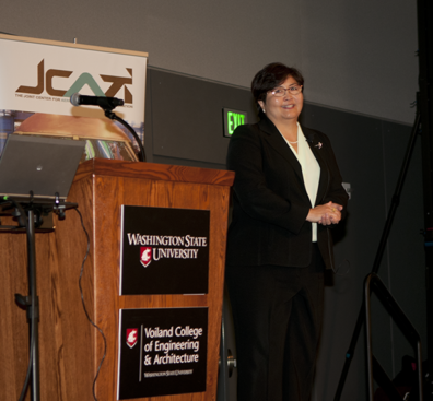 Iris Fujiura Bombelyn standing next to a podium in front of a JCATI banner.