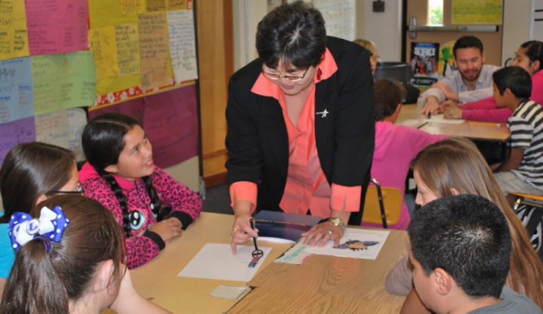 Iris Fujiura Bombelyn talks to elementary school children seated around a table.