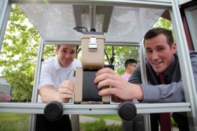Two men looking at the camera through a metal stand holding equipment.