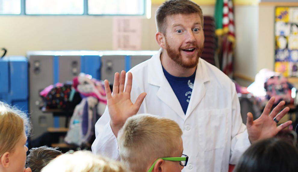 Brandon Clark wearing a lab coat and gesturing with his hands.