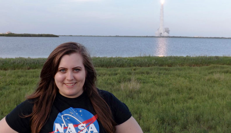 Amy Felt wearing a NASA t-shirt with a rocket launching in the background.