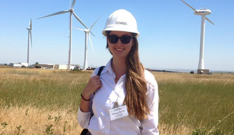Alyssa Norris standing near wind turbines while wearing a hard hat.