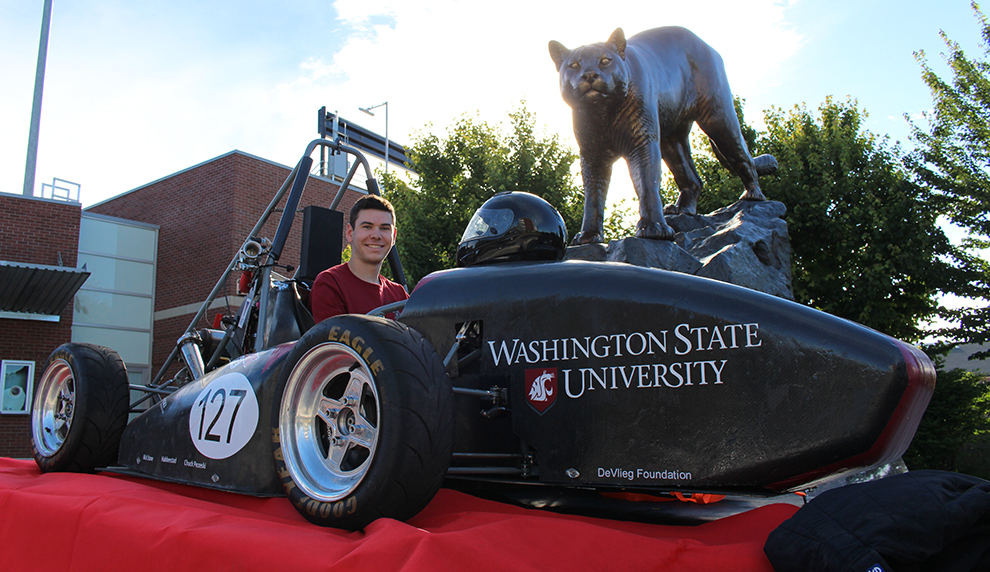 Kory O’Connor sits in WSU's Formula SAE race car next to WSU's bronze cougar statue.