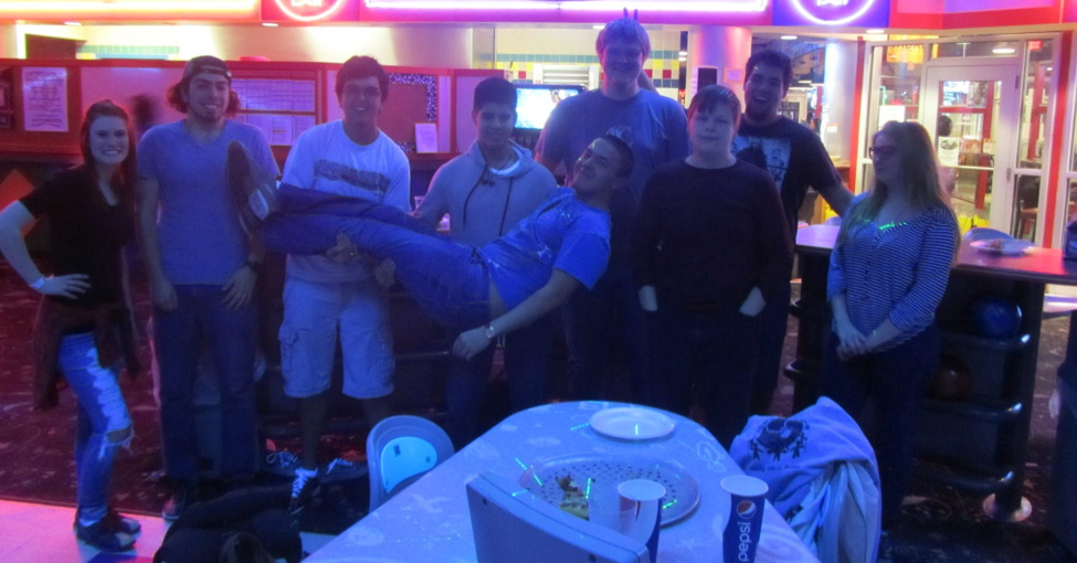 A man is lifted by two other men in a funny pose as several people look on.