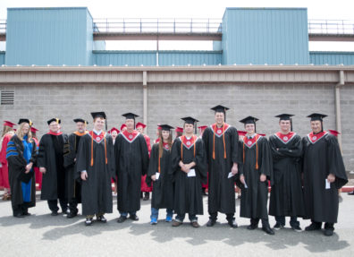 Graduates posing in a row wearing their caps and gowns.